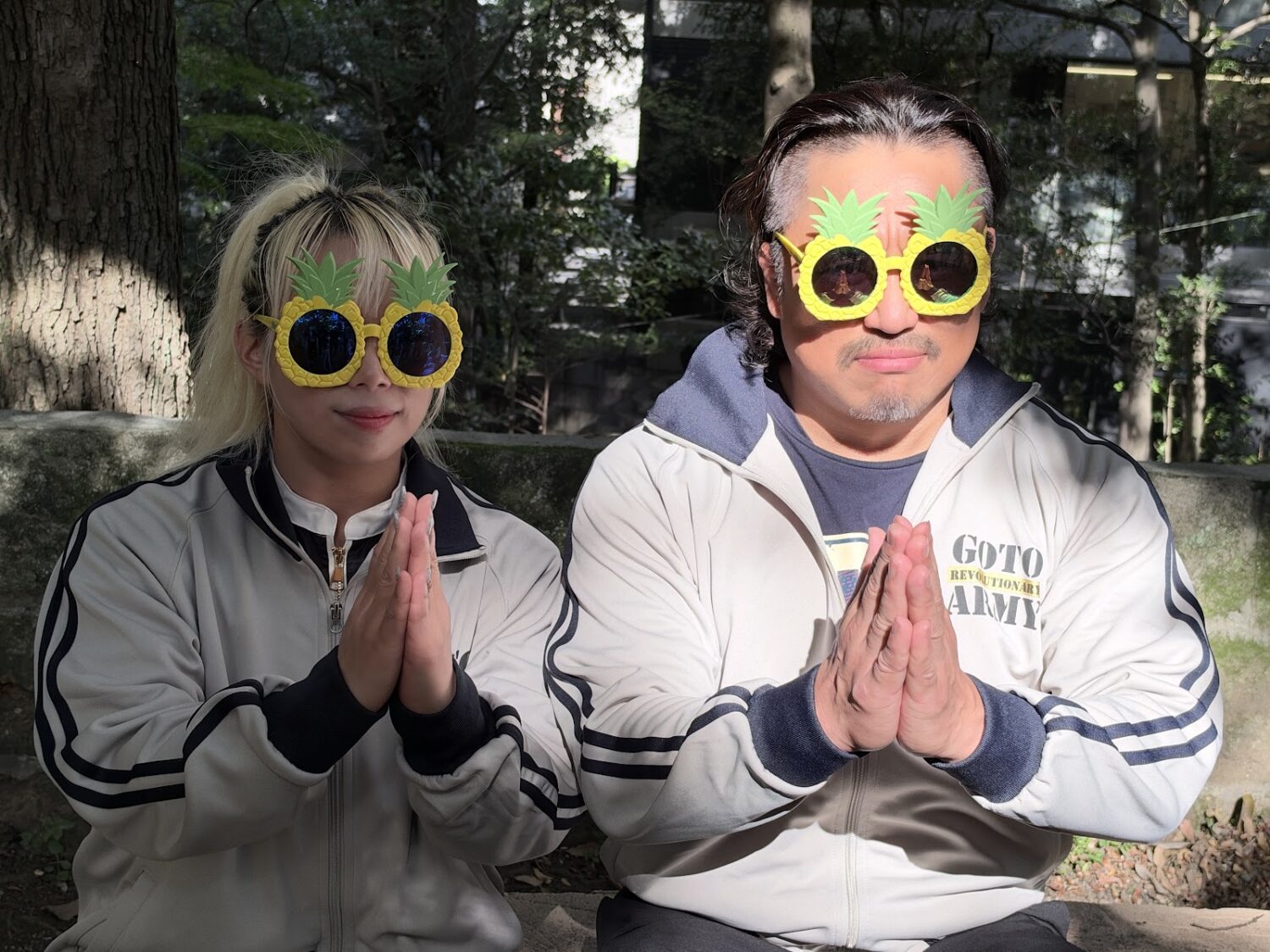 Yuna Mizumori and Hirooki Goto, both wearing pineapple-shaped sunglasses, clasp their hands together
